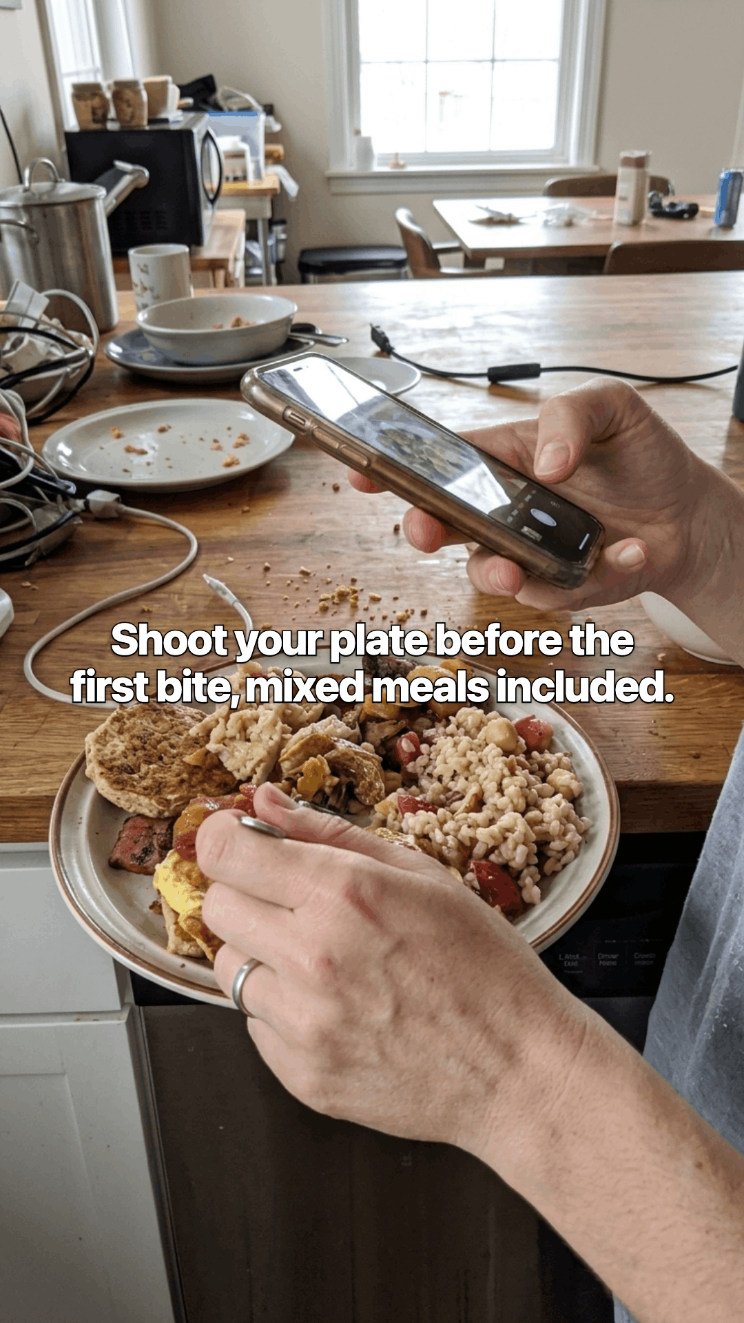 Two hands over a wooden counter, one holding a phone up to photograph a plate of food, with a line of the post across the photo.
