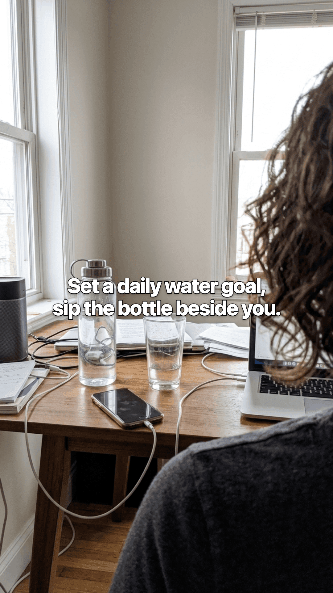 A desk by a window with a laptop, a water bottle and two glasses, seen over someone's shoulder, with a line of the post across the photo.